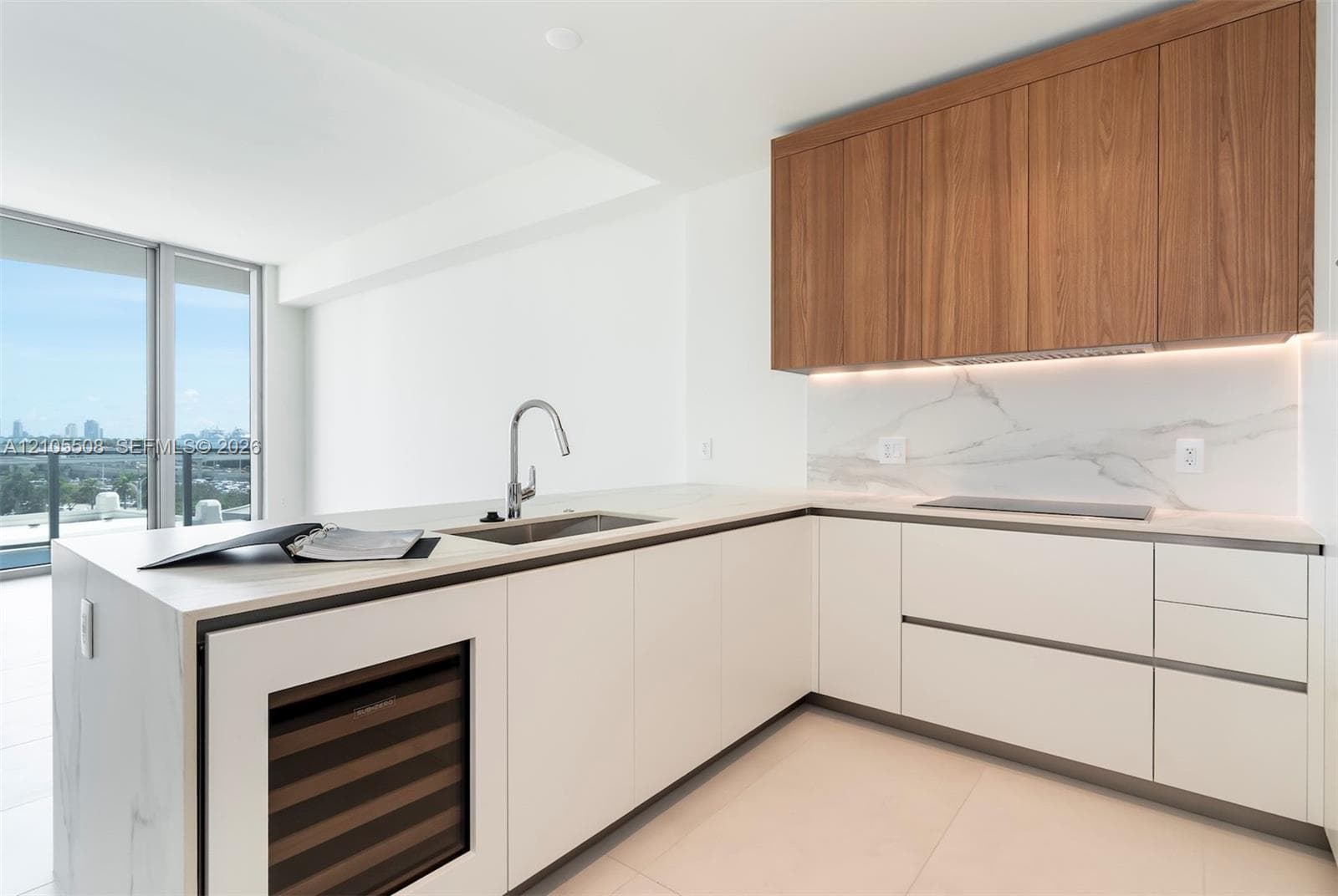 Modern kitchen featuring light wood-finish cabinetry, white flat-panel lower cabinetry, integrated stainless steel sink, under-cabinet lighting, and a built-in beverage cooler