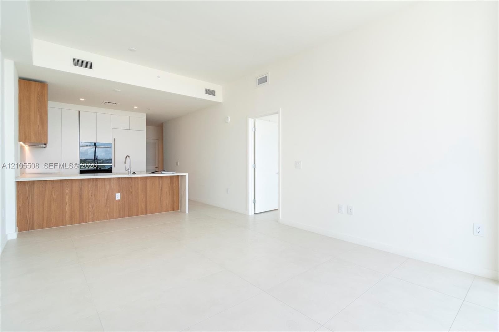 Open-concept living space featuring high ceilings, light tile flooring, built-in kitchen cabinetry with integrated appliances, and a kitchen island with a light-toned countertop