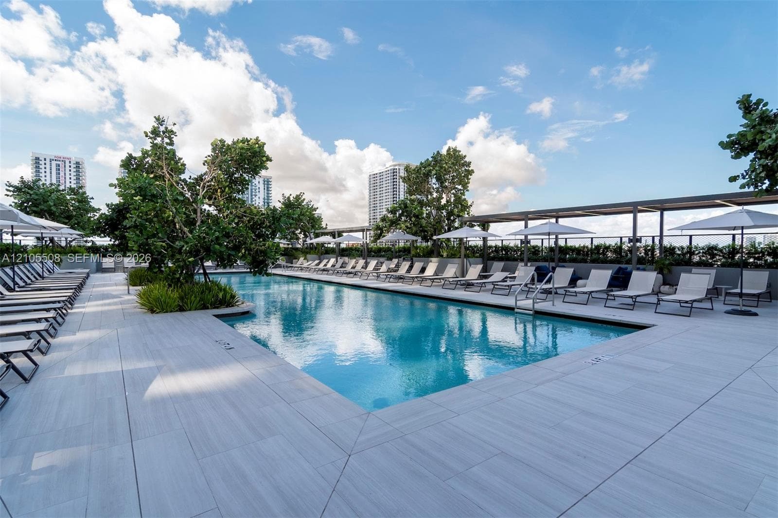 Resort-style pool with integrated steps, surrounded by large format tile decking, shaded lounge areas, and mature landscaping