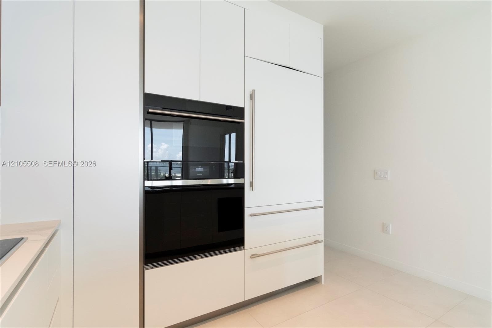 Integrated wall oven, white cabinetry, built-in refrigerator, sleek hardware, and light-toned tile flooring