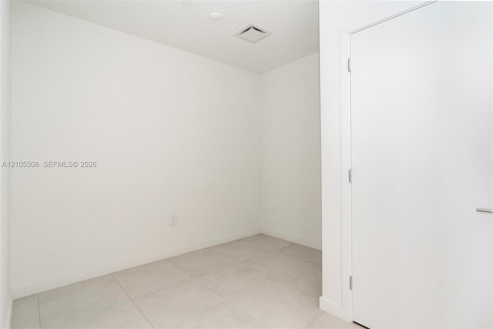 White ceramic tile flooring, recessed ceiling lighting, and a flush-mounted door with a modern handle