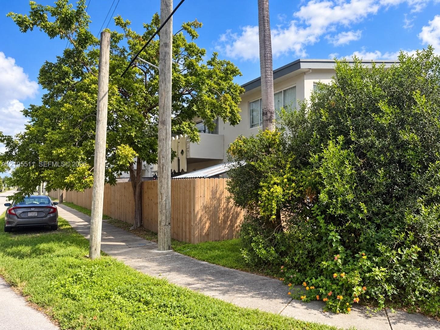 Two-story exterior featuring a flat roofline, neutral facade, wood privacy fencing, and mature landscaping