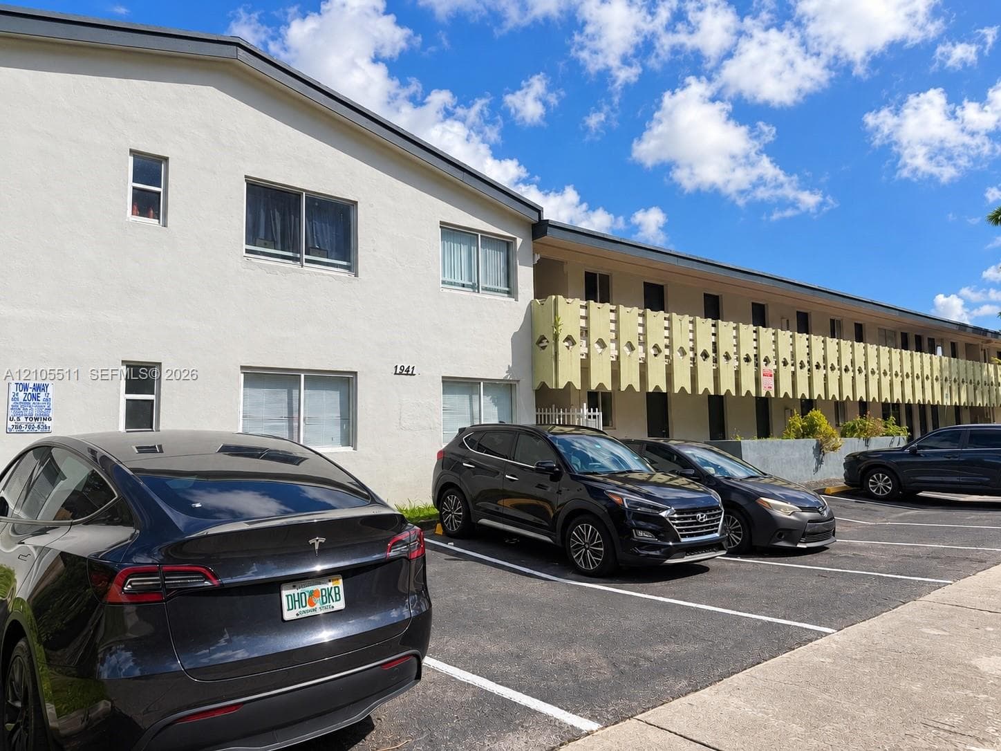 Exterior facade featuring light-colored stucco siding, a decorative balcony screen, and asphalt surface parking