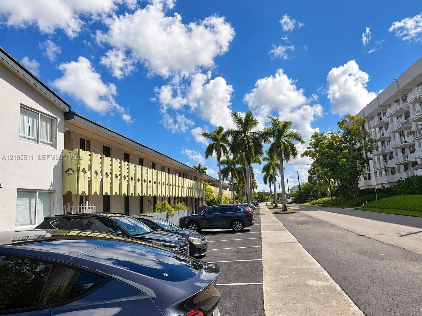 Exterior facade featuring decorative balcony screens, paved parking area, and mature palm trees