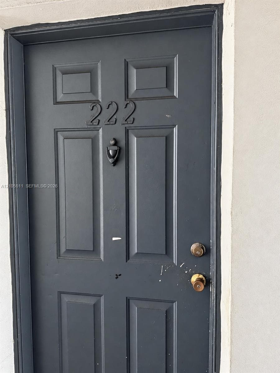 Dark gray six-panel door featuring metallic address numerals, a mounted door knocker, and dual-locking hardware