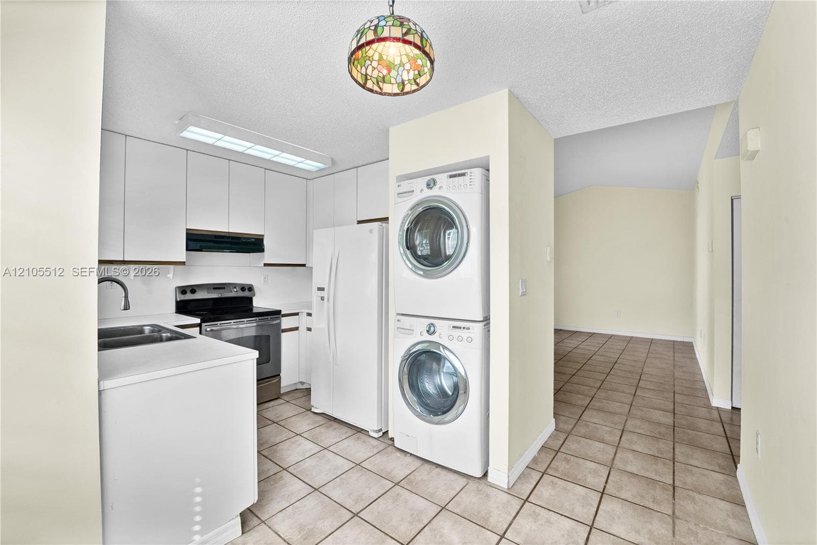 Kitchen featuring white cabinetry, stainless steel appliances, dual-basin sink with a gooseneck faucet, tile flooring, and a stained-glass pendant light fixture