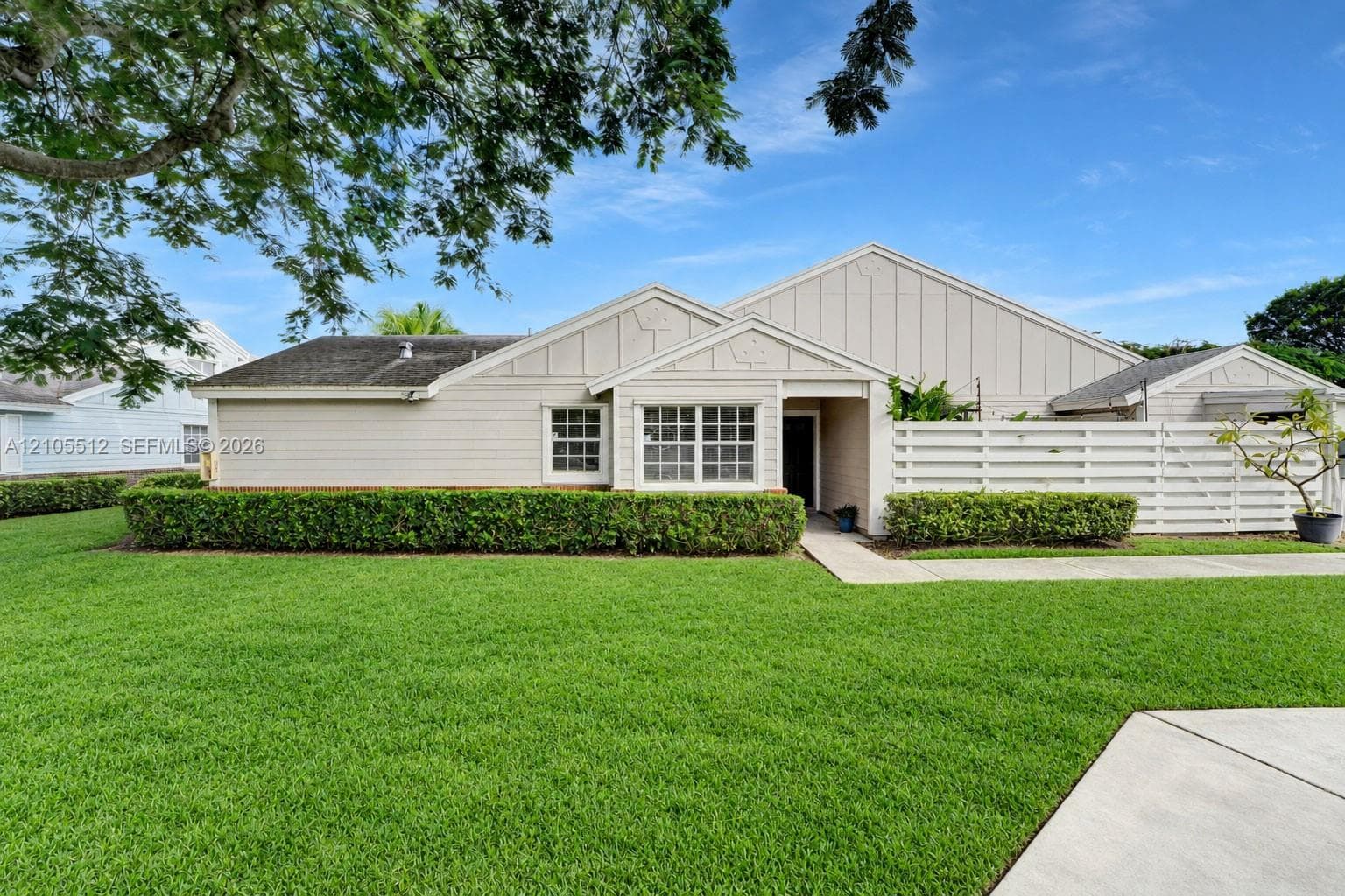 Single-story exterior featuring light-toned horizontal siding, multi-gabled rooflines, decorative gable accents, a concrete walkway, and a private white slatted fence