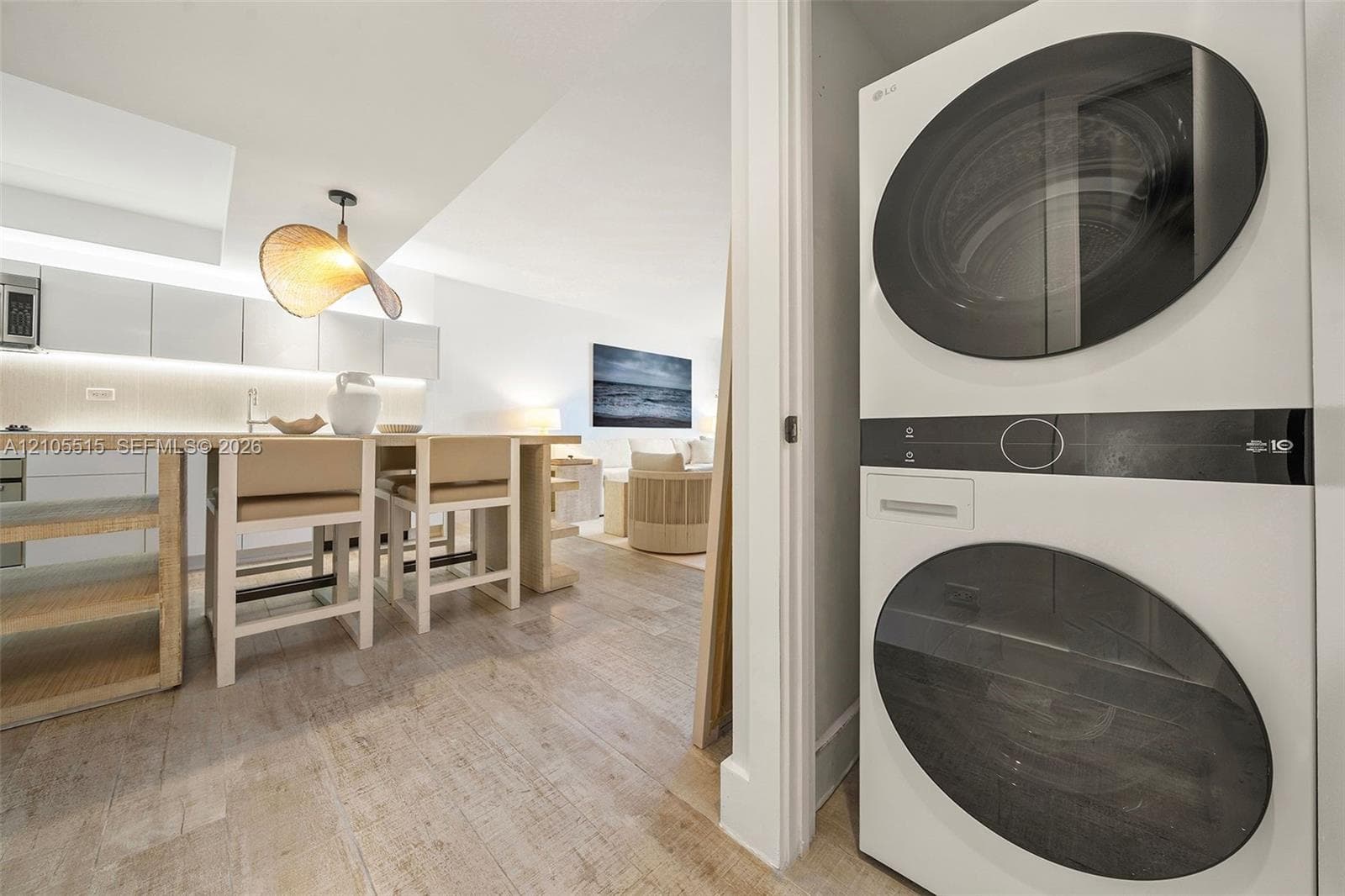 Stacked white laundry unit with round glass-front doors, featuring integrated kitchen cabinetry, wood-finish flooring, and a contemporary pendant lighting fixture