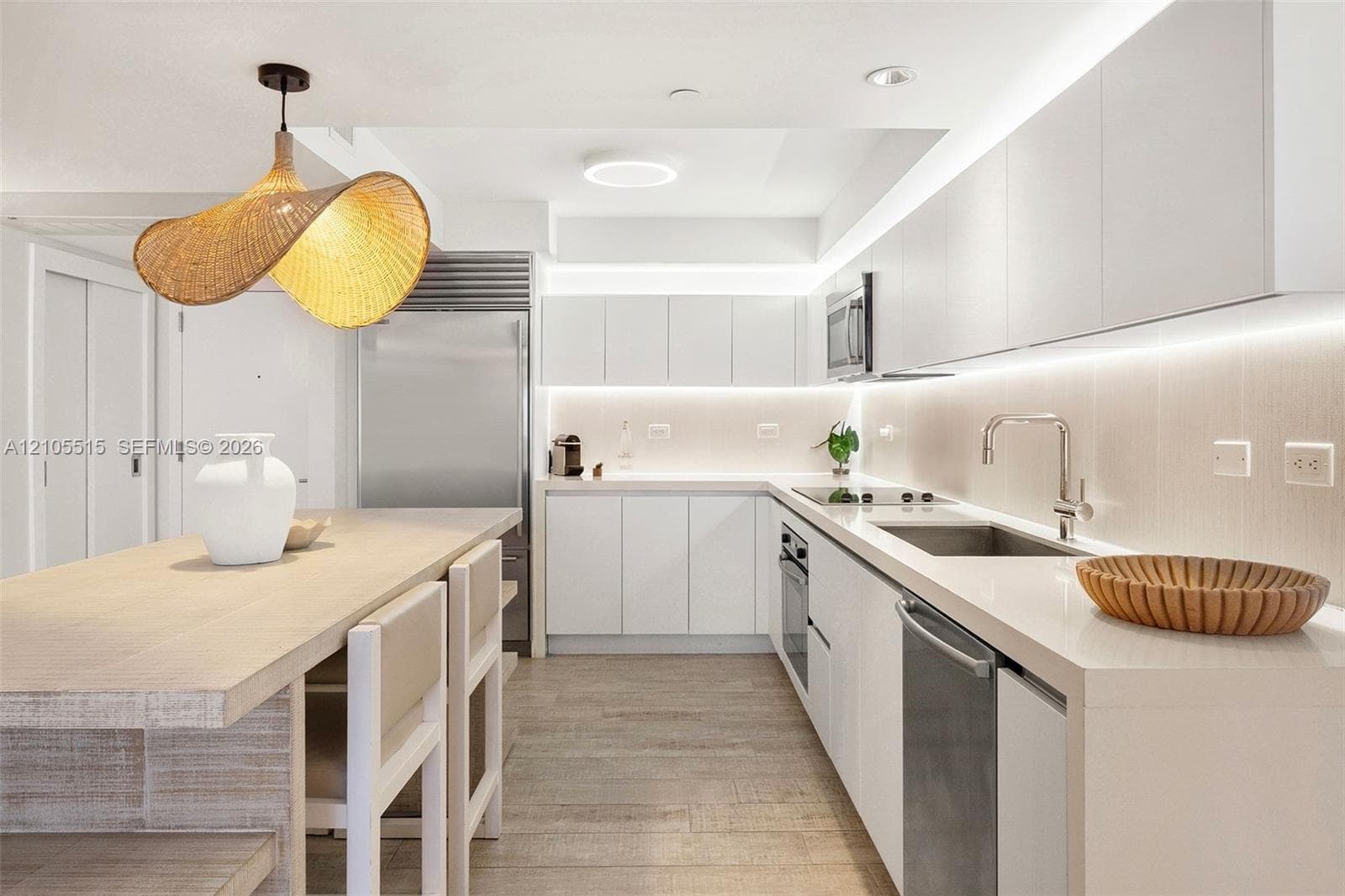 Contemporary kitchen featuring flat-panel white cabinetry, stone-surface countertops, under-cabinet lighting, stainless steel appliances, and wood-finish flooring