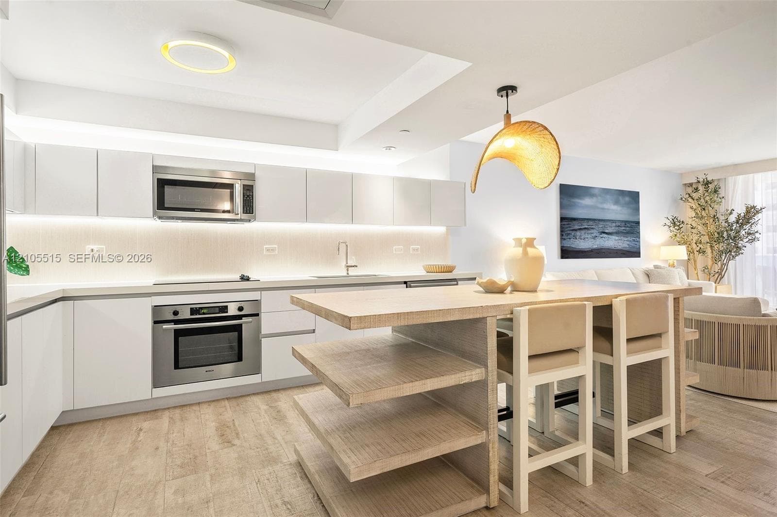 Kitchen featuring white flat-panel cabinetry, stainless steel appliances, under-cabinet lighting, wood-finish flooring, and a central island with built-in shelving