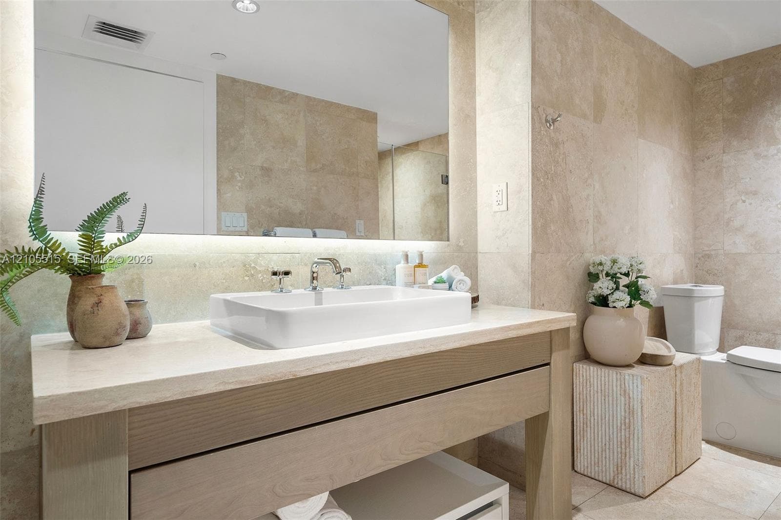 Bathroom featuring a stone-topped wood vanity, rectangular vessel sink, wall-spanning mirror with integrated under-lighting, and floor-to-ceiling stone tile wall finishes