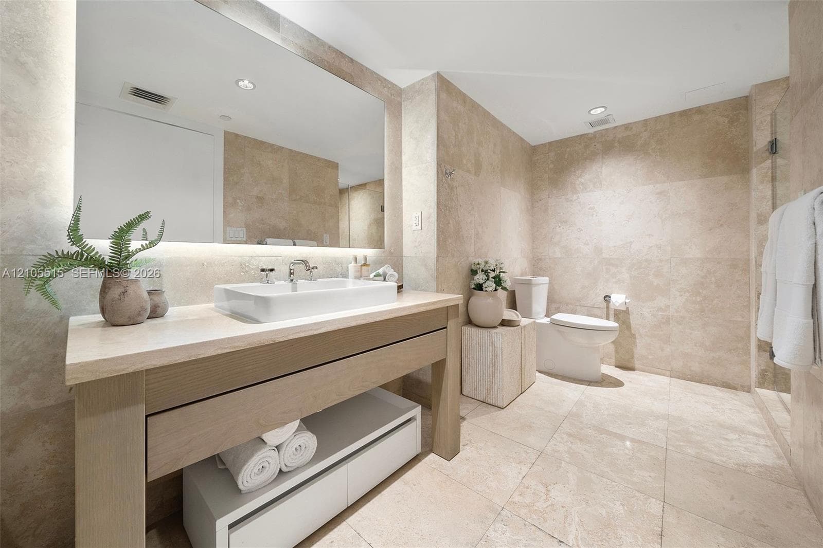 Bathroom featuring floor-to-ceiling stone-tile walls, oversized vanity with an integrated basin, under-cabinet storage, and full-width wall mirror with integrated lighting