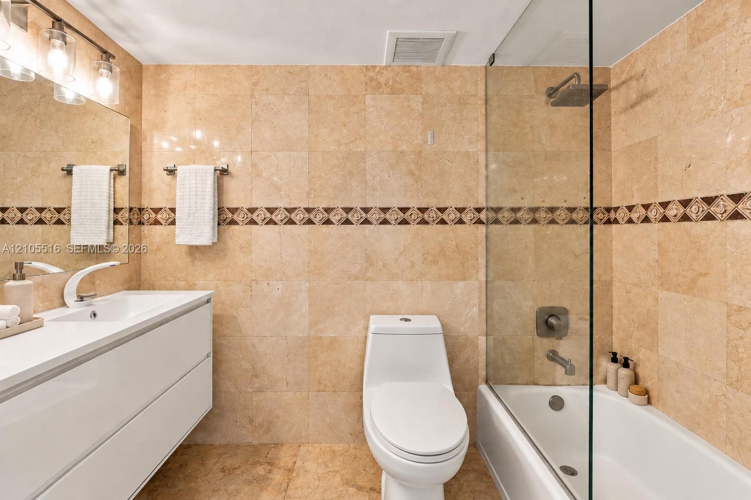 Bathroom featuring full-height stone-finish wall tile, a frameless glass shower panel, a wall-mounted vanity with integrated sink, and a modern light fixture