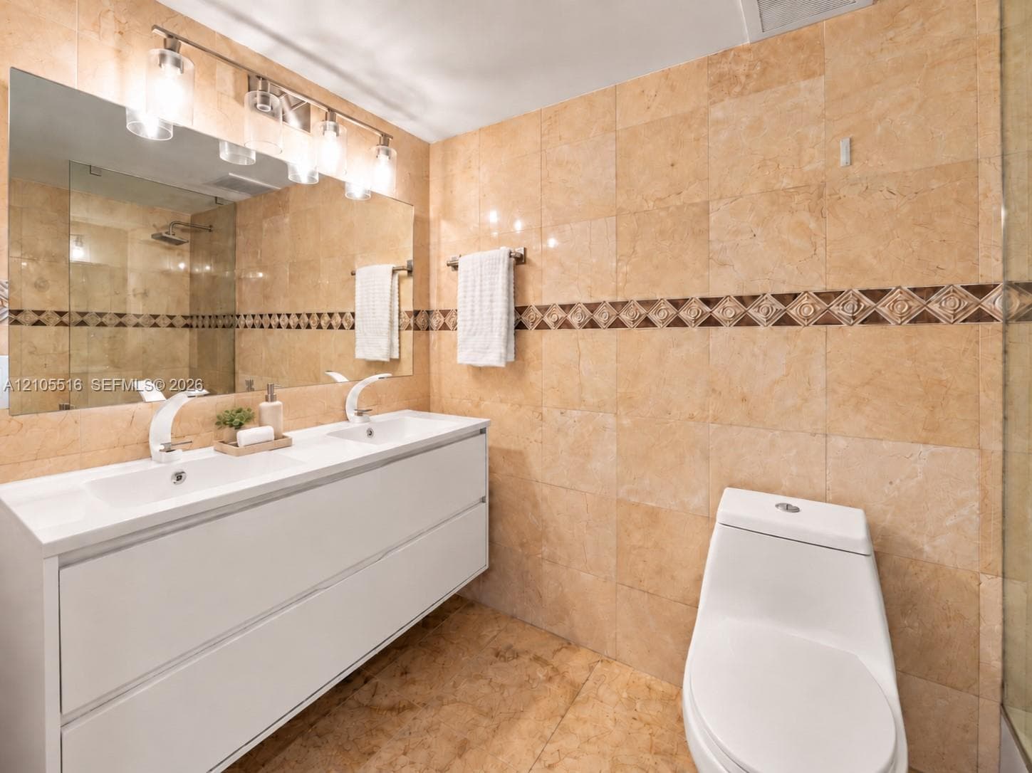 Dual vanity with integrated sinks, full-width mirror, sconce lighting, and decorative accent tile