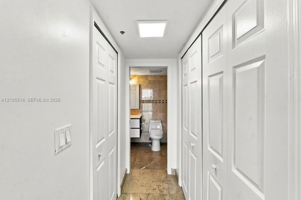 Hallway with white panel doors, overhead square light fixture, and tile flooring