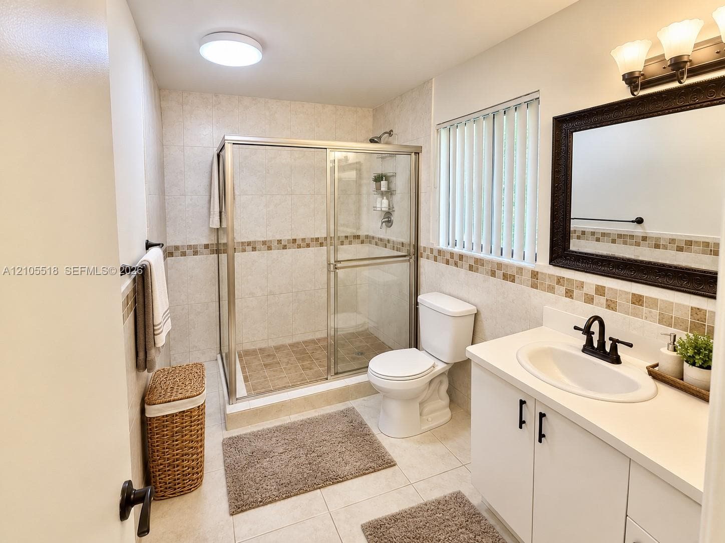 Bathroom featuring a walk-in shower with glass enclosure, white vanity cabinet, solid-surface countertop with integrated sink, tile wall accents, and vanity lighting