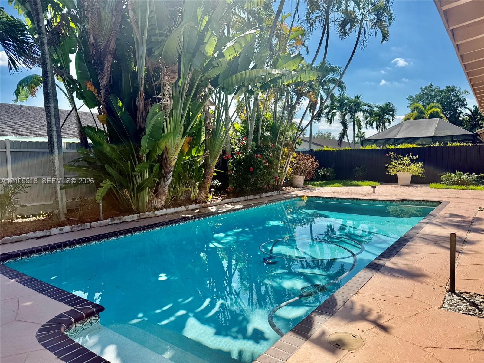 In-ground swimming pool featuring a dark tile border, paved decking, and established tropical landscaping