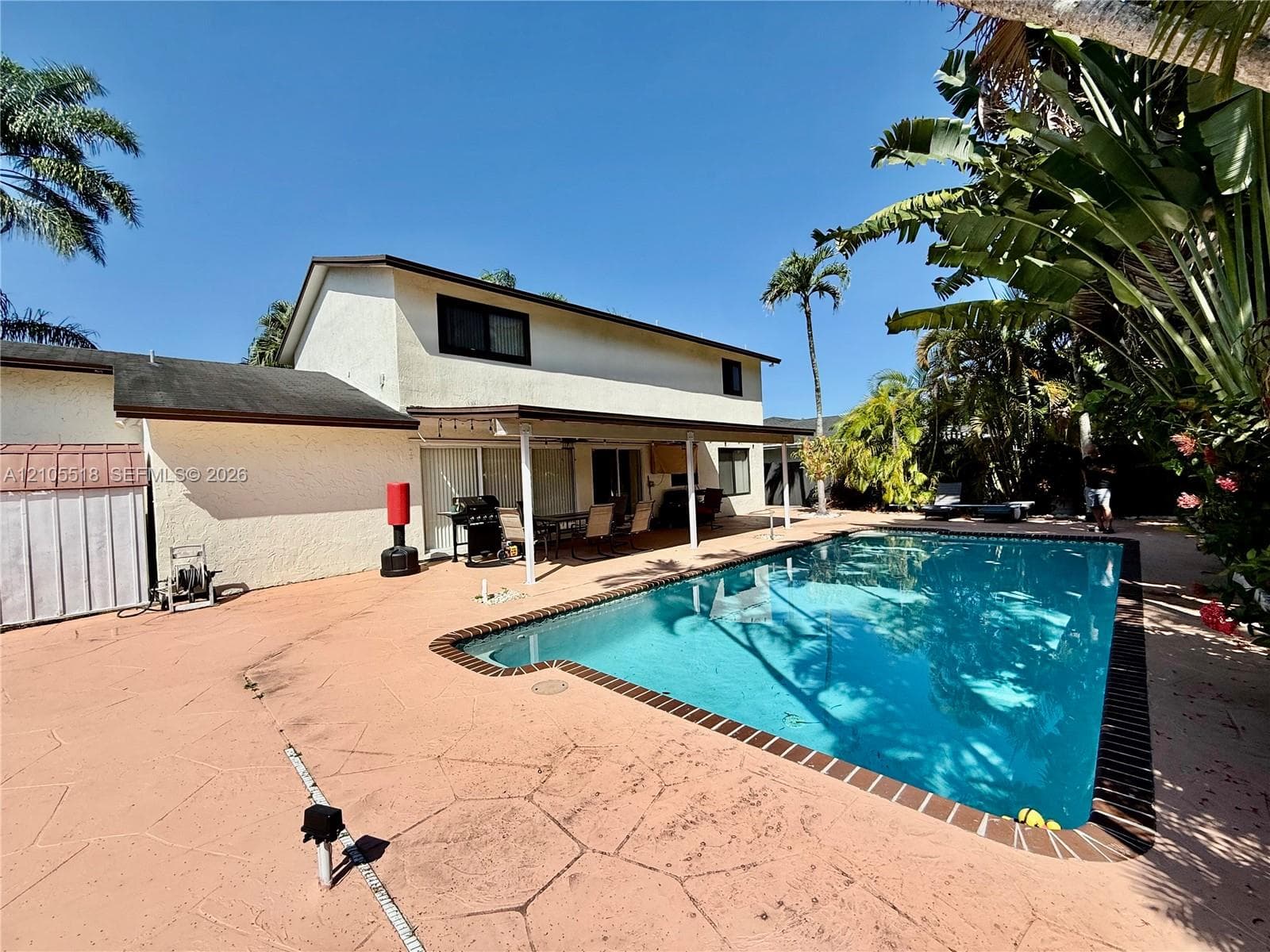 Backyard featuring an inground swimming pool, concrete patio, covered patio area, and mature tropical landscaping