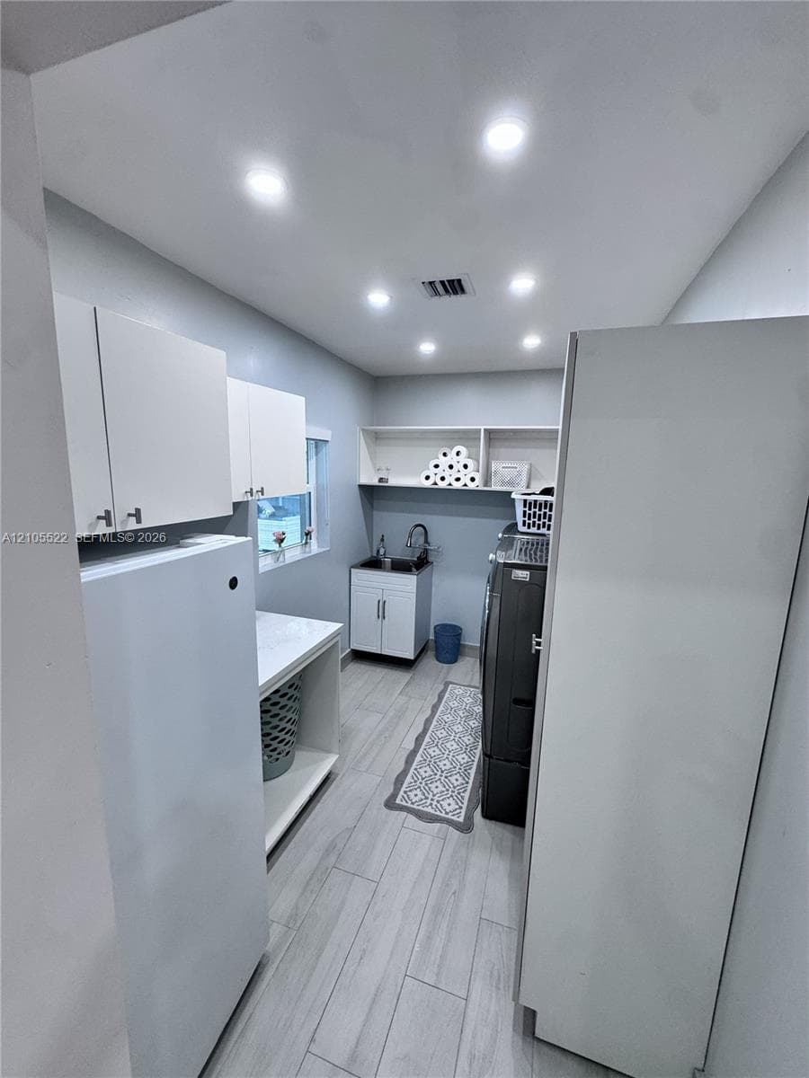 Recessed lighting, wood-finish flooring, built-in shelving, white cabinetry, and a utility sink