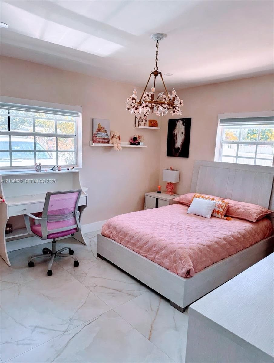 Recessed lighting, ornate chandelier, large windows with white trim, white desk with integrated shelving, and white tile flooring