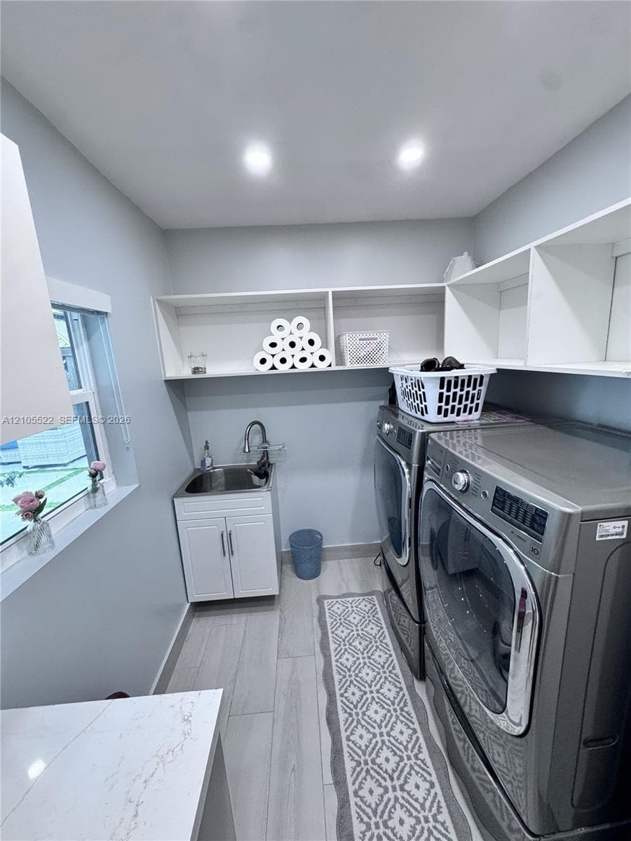Laundry space featuring wood-finish flooring, built-in shelving, a utility sink with cabinetry, and a window