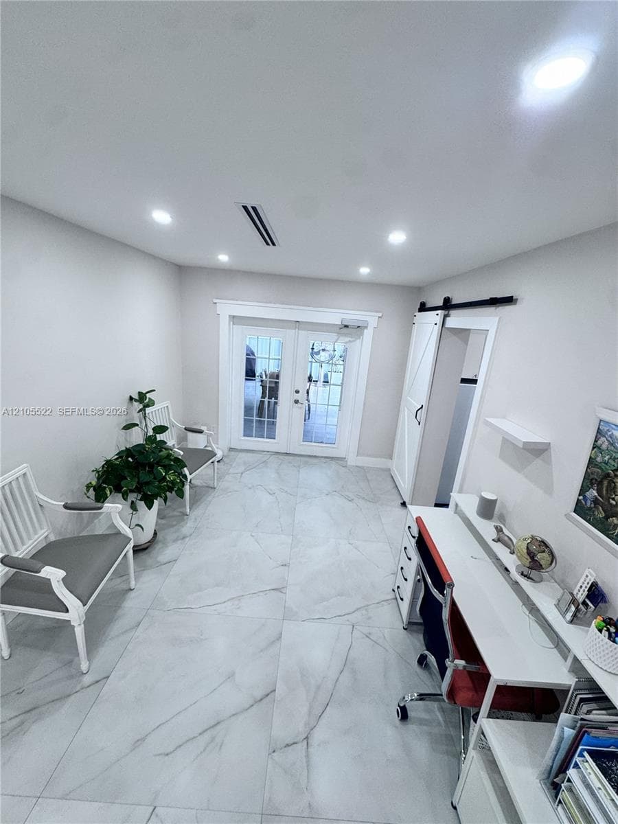 Recessed lighting illuminates the space, featuring large format tile flooring and white french doors