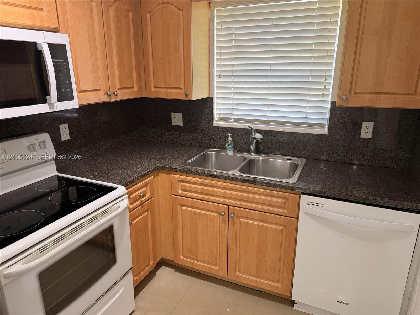 Wood-finish cabinetry, dark countertops, and stainless steel double basin sink