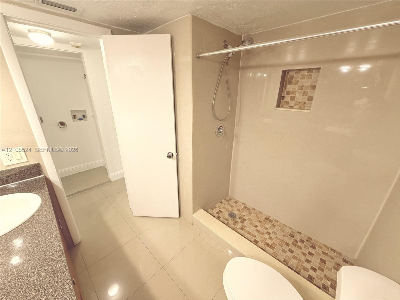 Walk-in shower with mosaic tile floor and recessed shelf, vanity with undermount sink and stone-finish countertop, and tile flooring throughout