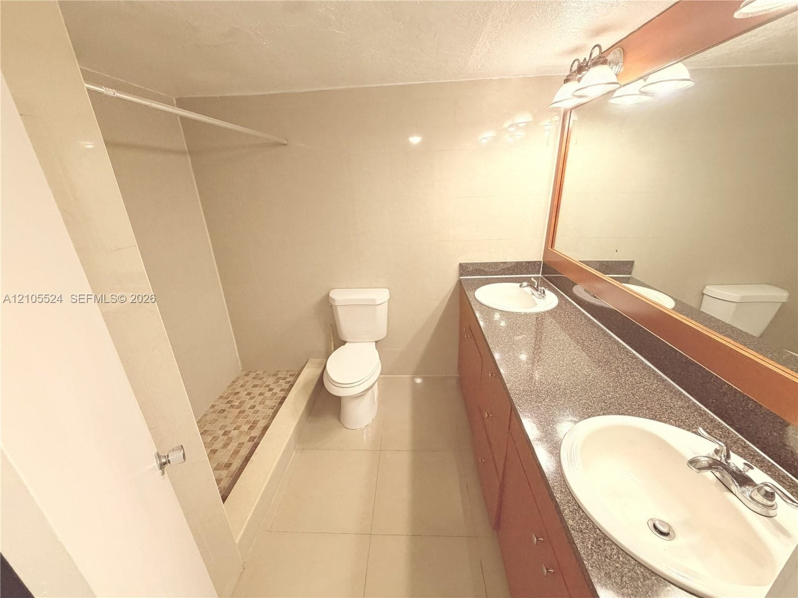 Dual vanity with integrated sinks, wood-finish cabinetry, a large mirrored wall, and a three-light fixture