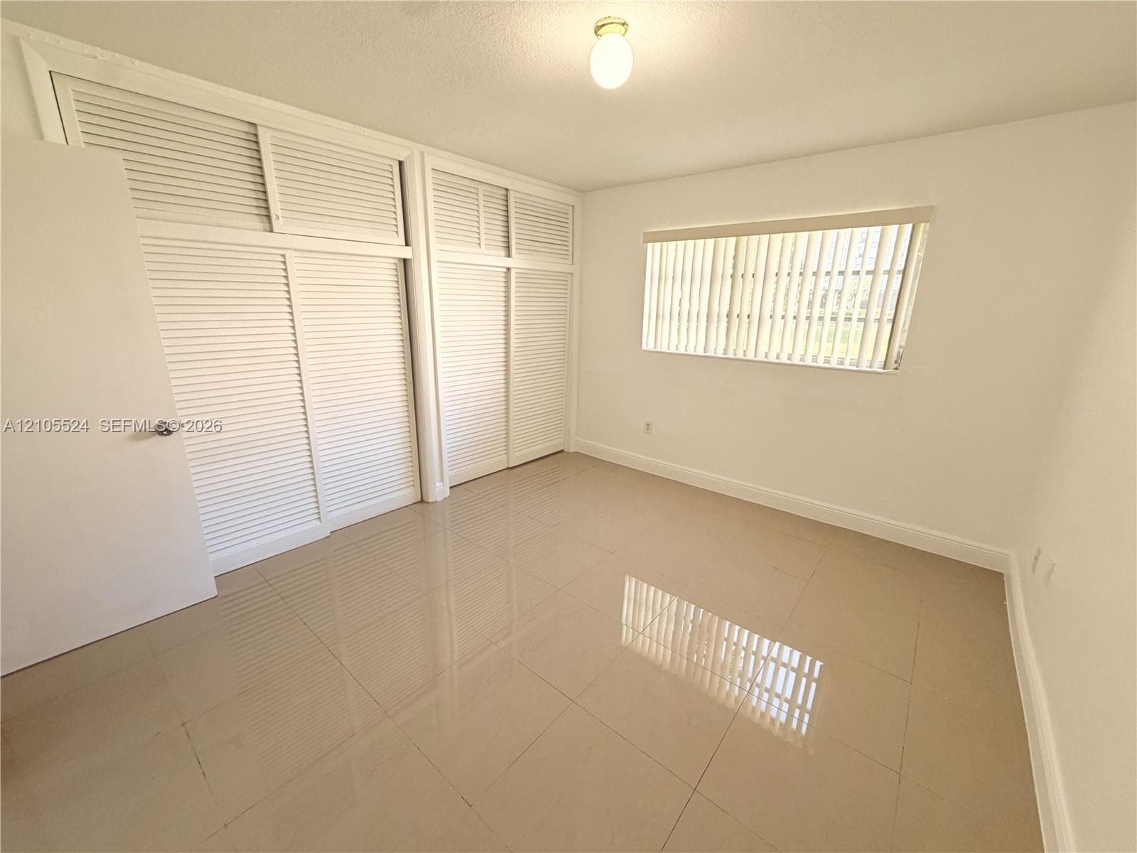 Spacious interior featuring louvered closet doors, a single window with blinds, and polished tile flooring