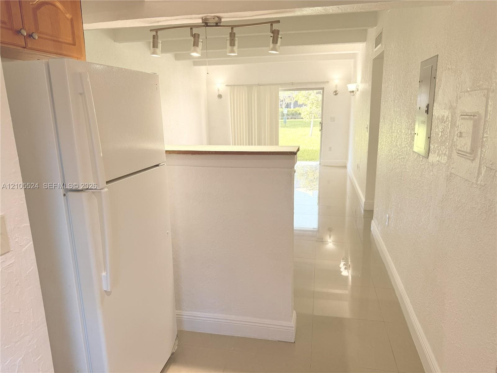White refrigerator, track lighting, light wood-finish cabinetry, tile flooring, and a sliding glass door
