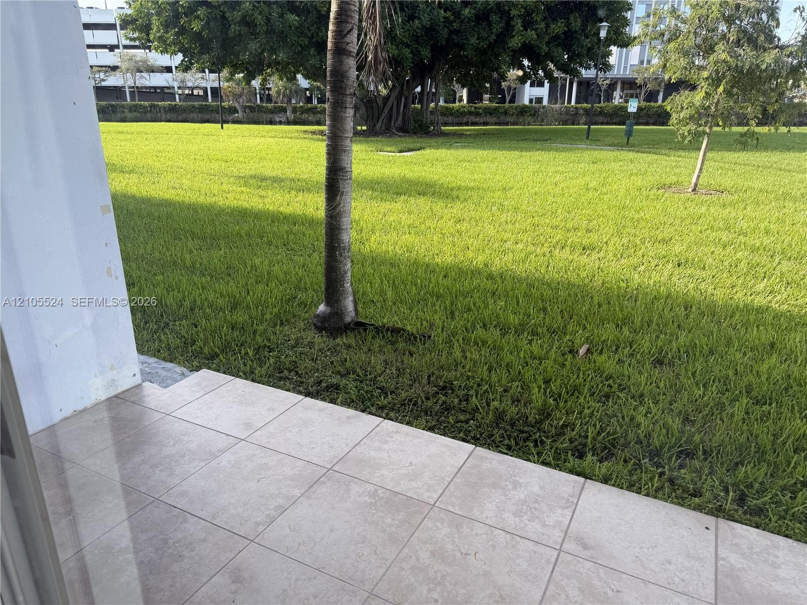 Tiled patio with a broad expanse of green lawn, featuring mature trees and distant buildings