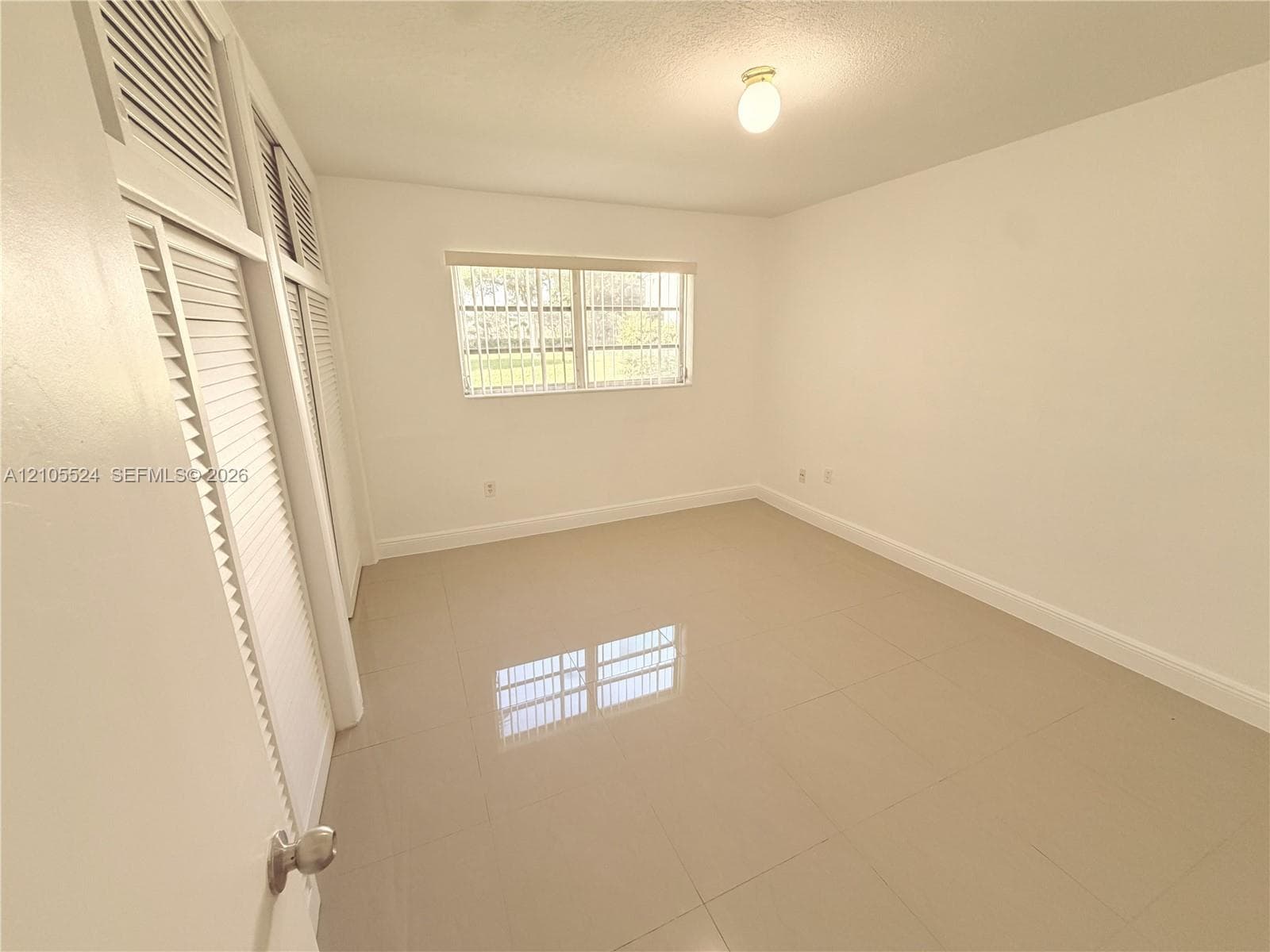 White walls, tile flooring, window with vertical blinds, and louvered bifold closet doors