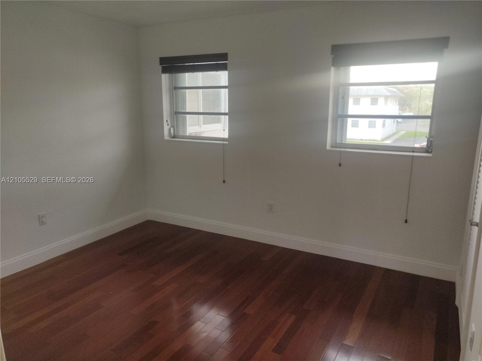 Hardwood flooring, painted walls, two windows, two window coverings, and white trim