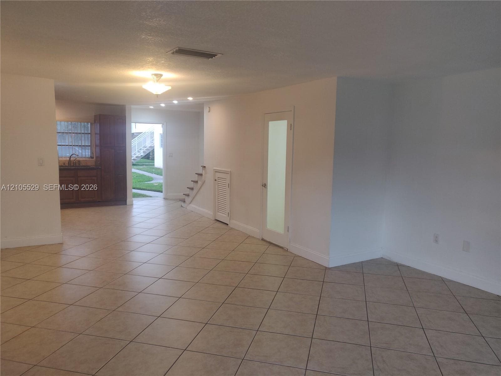 Tile flooring throughout, recessed lighting, and a kitchen area featuring wood cabinetry, a sink, and a window