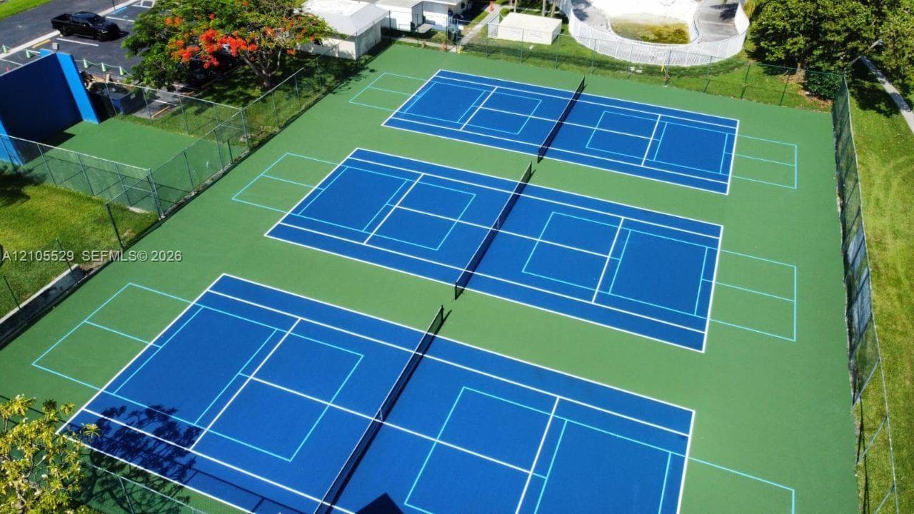 Three blue-surfaced courts with white boundary lines, green surrounding surface, and perimeter fencing