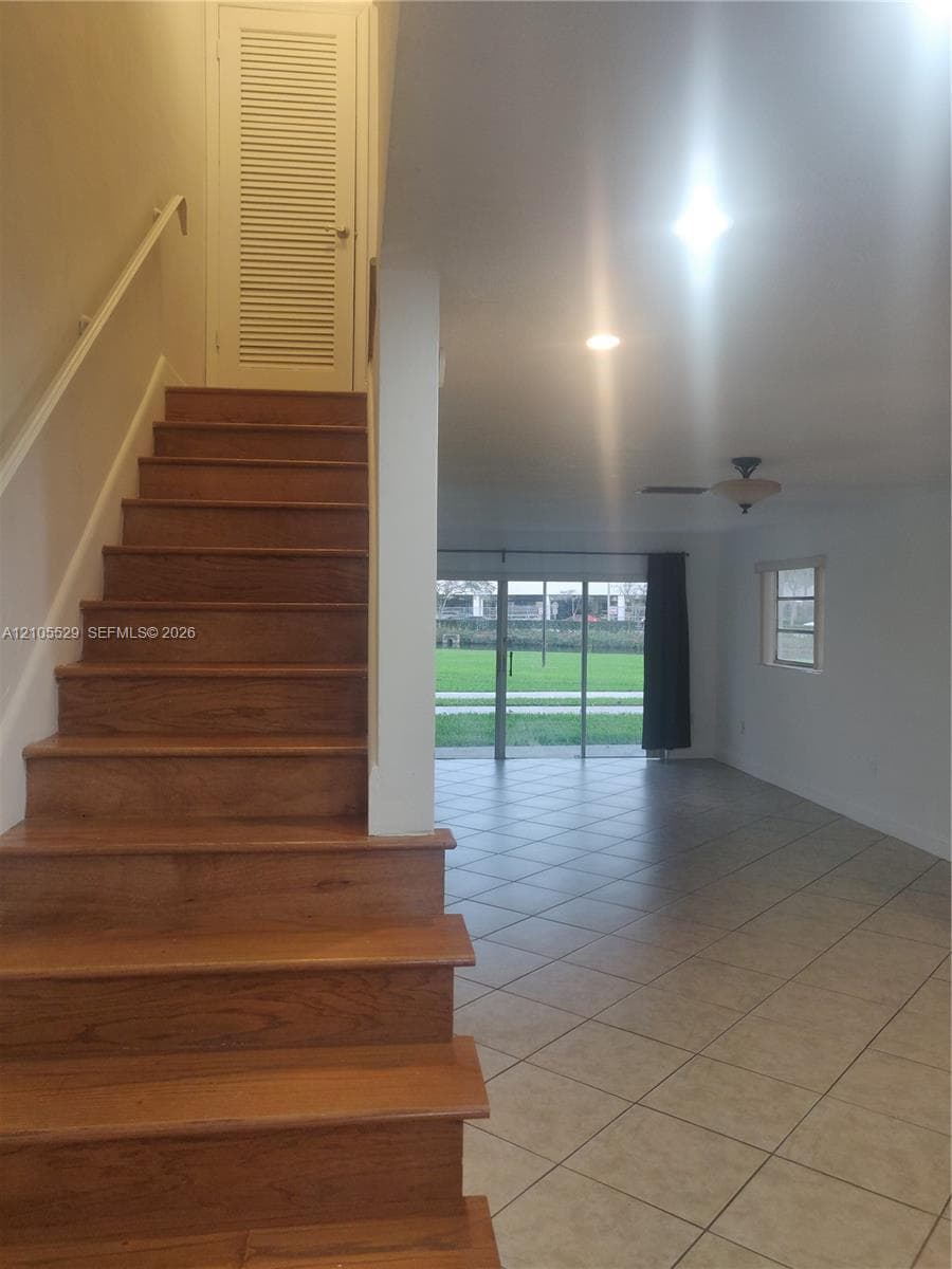 Wood-finish staircase with white handrail, recessed lighting, and tile flooring