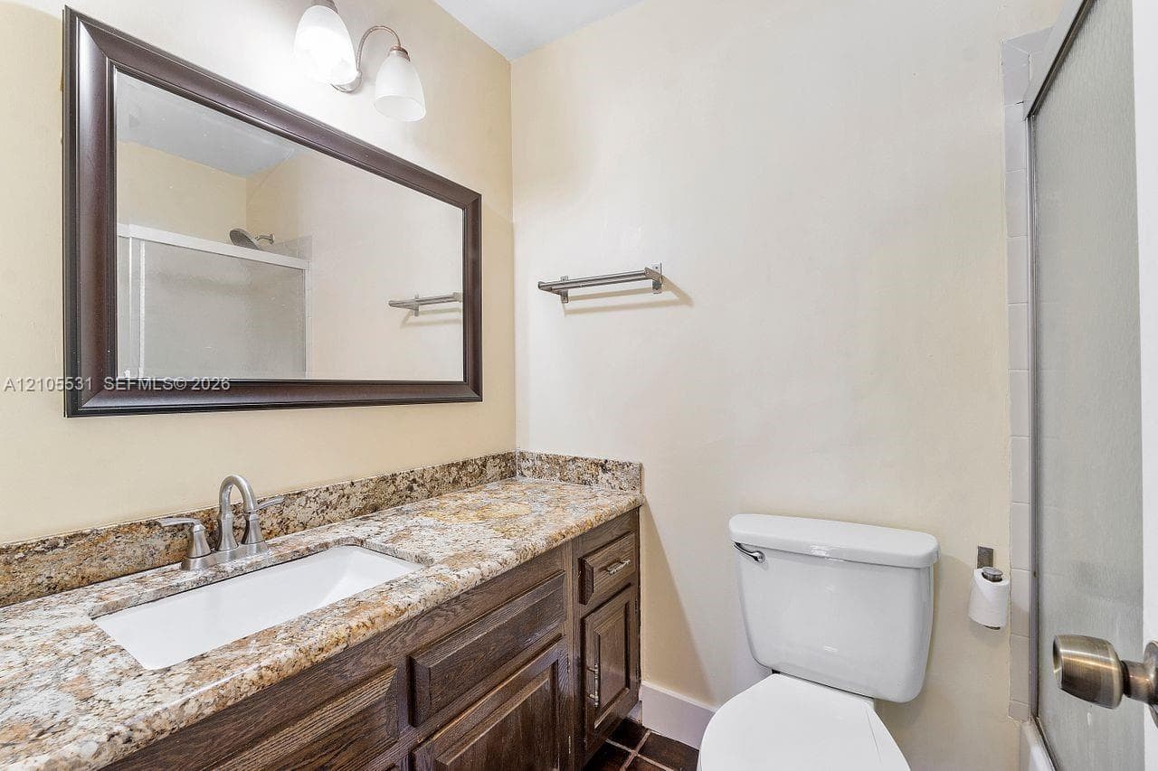 Vanity with a granite-style countertop, undermount sink, and wood-finish cabinetry