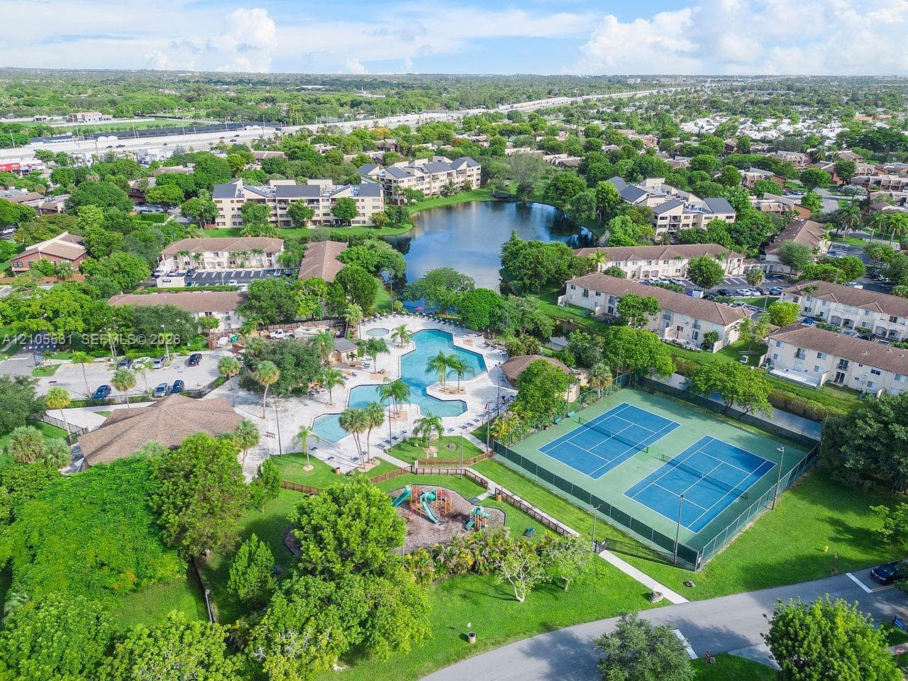 Community featuring multiple swimming pools, tennis courts, and a playground, surrounded by mature landscaping and a central pond
