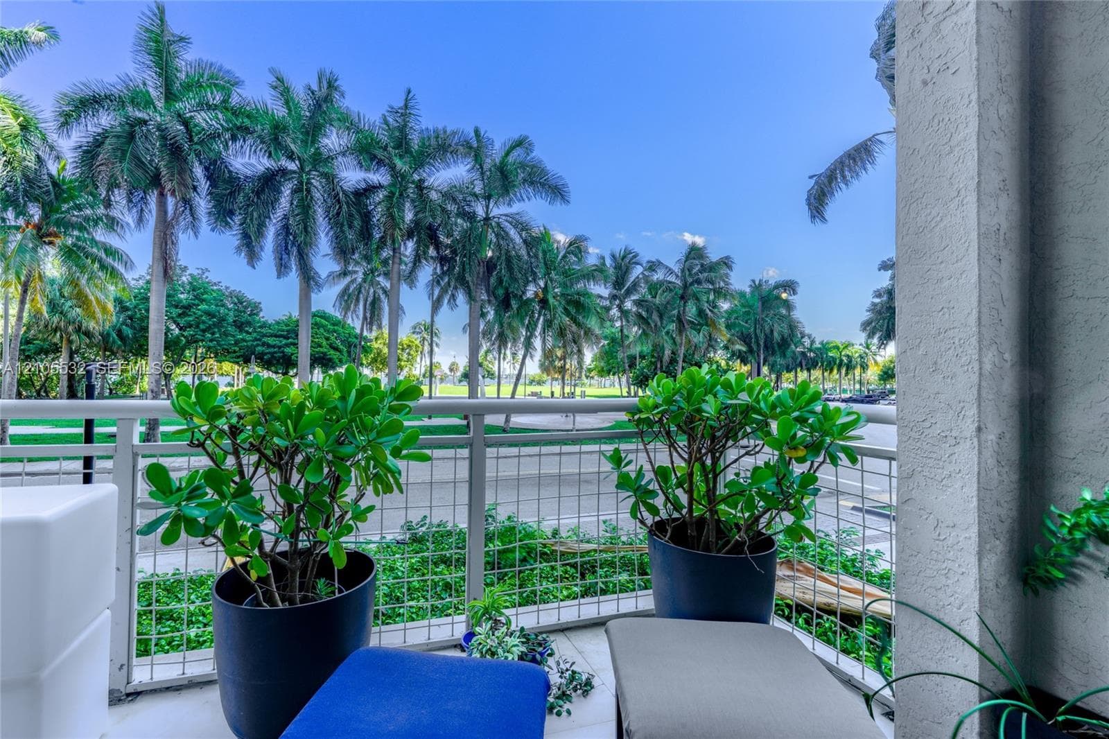 Covered balcony with white metal lattice railing, tiled flooring, and mature palm tree scenery