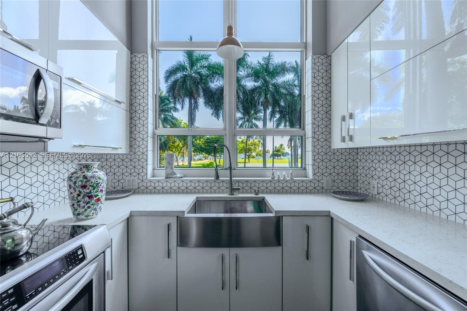 Kitchen featuring high-gloss cabinetry, stone-finish countertops, stainless steel farmhouse sink, and geometric-patterned backsplash tile, accented by a floor-to-ceiling window