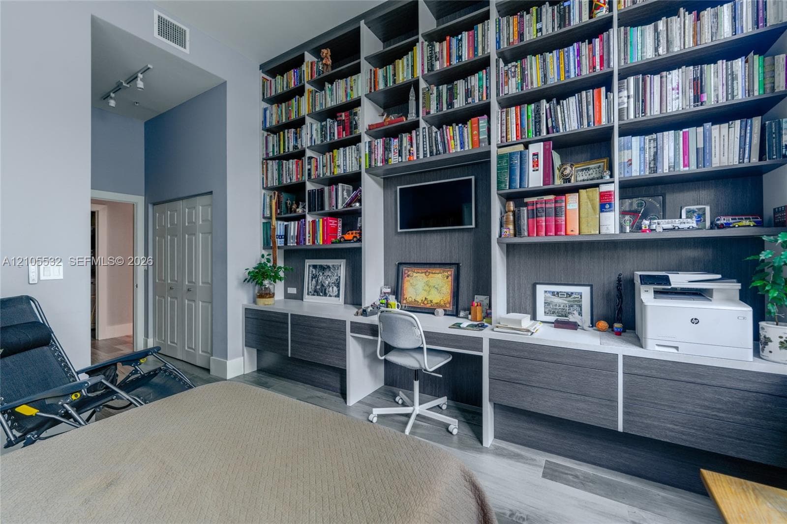 Floor-to-ceiling custom built-in shelving, integrated desk workspace, dual-tone cabinetry with wood-finish detailing, track lighting, and wood-finish flooring