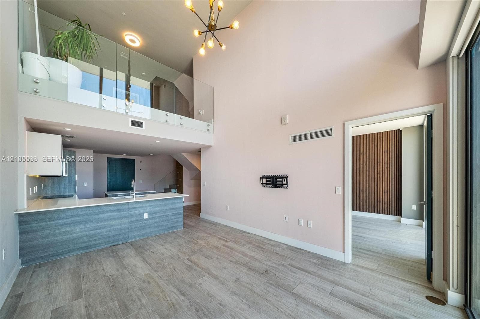 Double-height ceiling, glass-paneled mezzanine railing, wood-finish flooring, kitchen island with solid surface countertop, and modern multi-arm pendant lighting