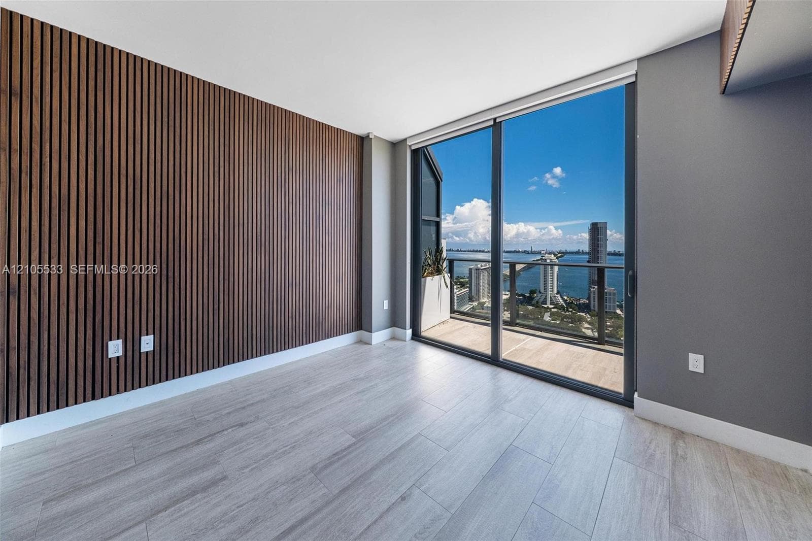 Wood-slat accent wall, tile flooring, floor-to-ceiling glass sliding doors, and private balcony with water and city skyline