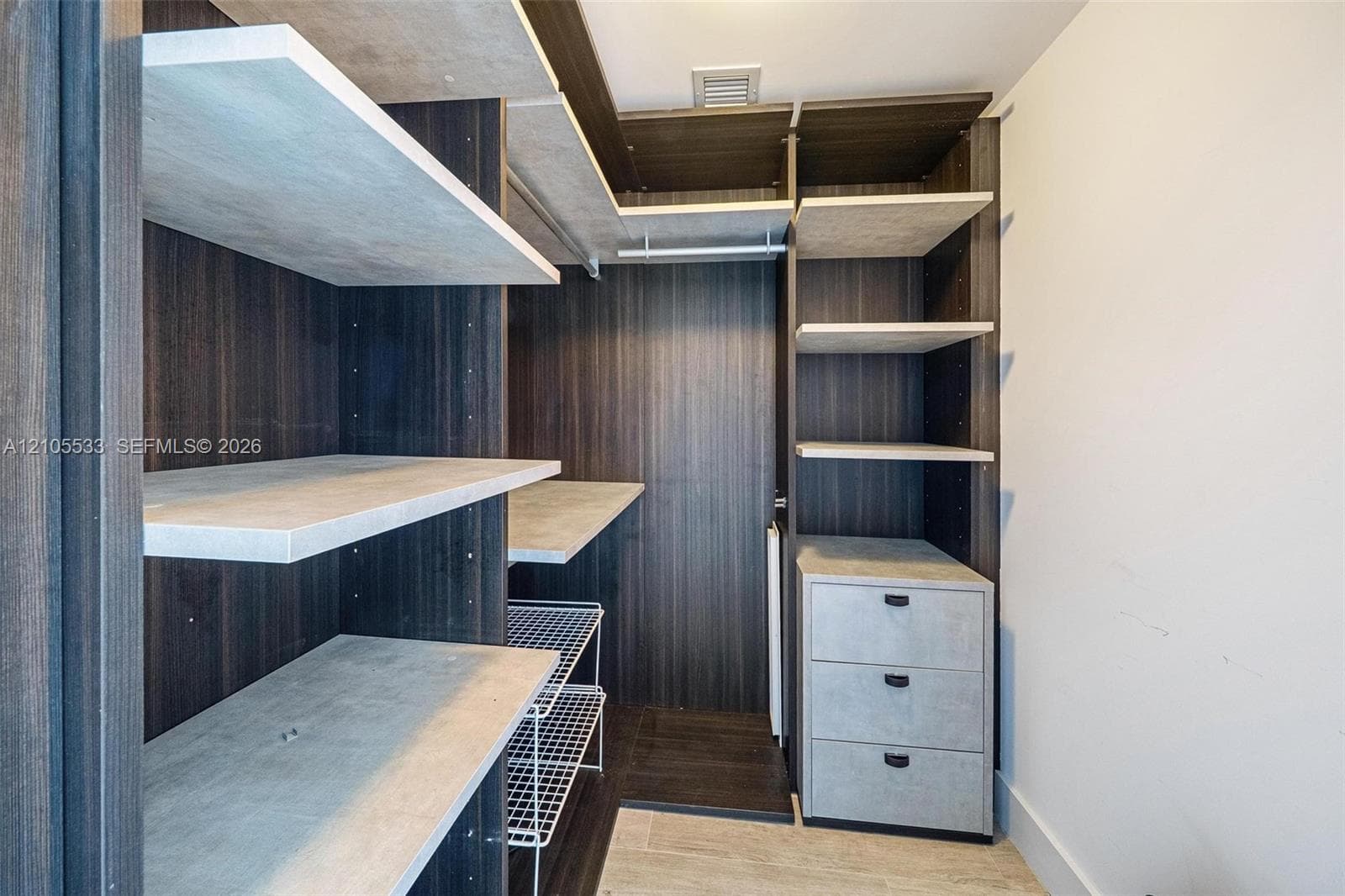 Custom walk-in closet featuring dark wood-finish cabinetry, light-toned open shelving, integrated three-drawer dresser unit, and wire storage racks