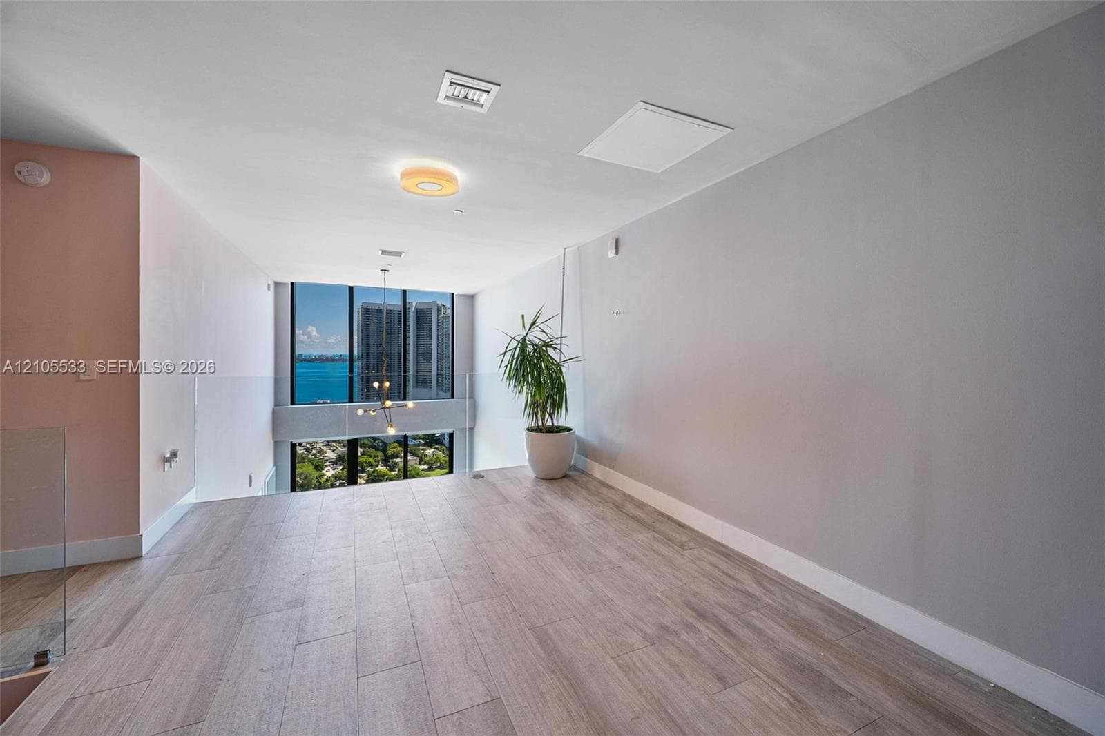 Open-plan interior featuring wood-finish flooring, floor-to-ceiling windows, and a glass panel railing