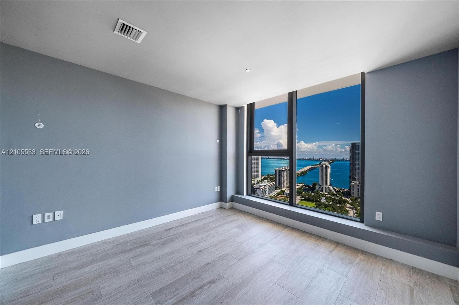 Floor-to-ceiling windows, wood-finish flooring, and expansive water and urban surroundings