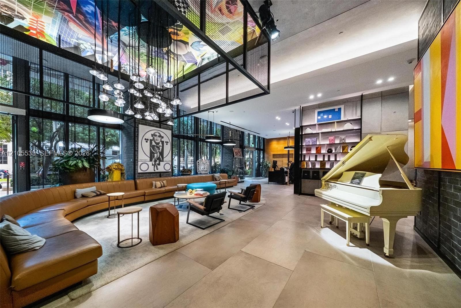 Expansive lobby featuring floor-to-ceiling windows, large-format tile flooring, industrial-style grid ceiling structure with integrated lighting, and built-in floor-to-ceiling shelving