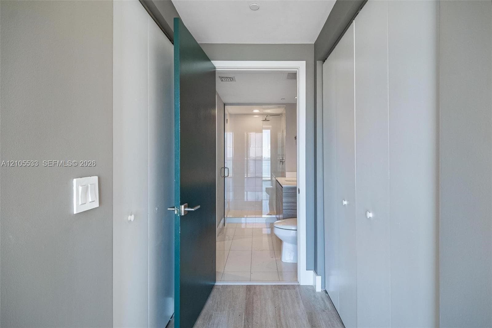 Entryway featuring wood-finish flooring, dual built-in closets with knob hardware, and a solid-core interior door leading to a tiled bathroom