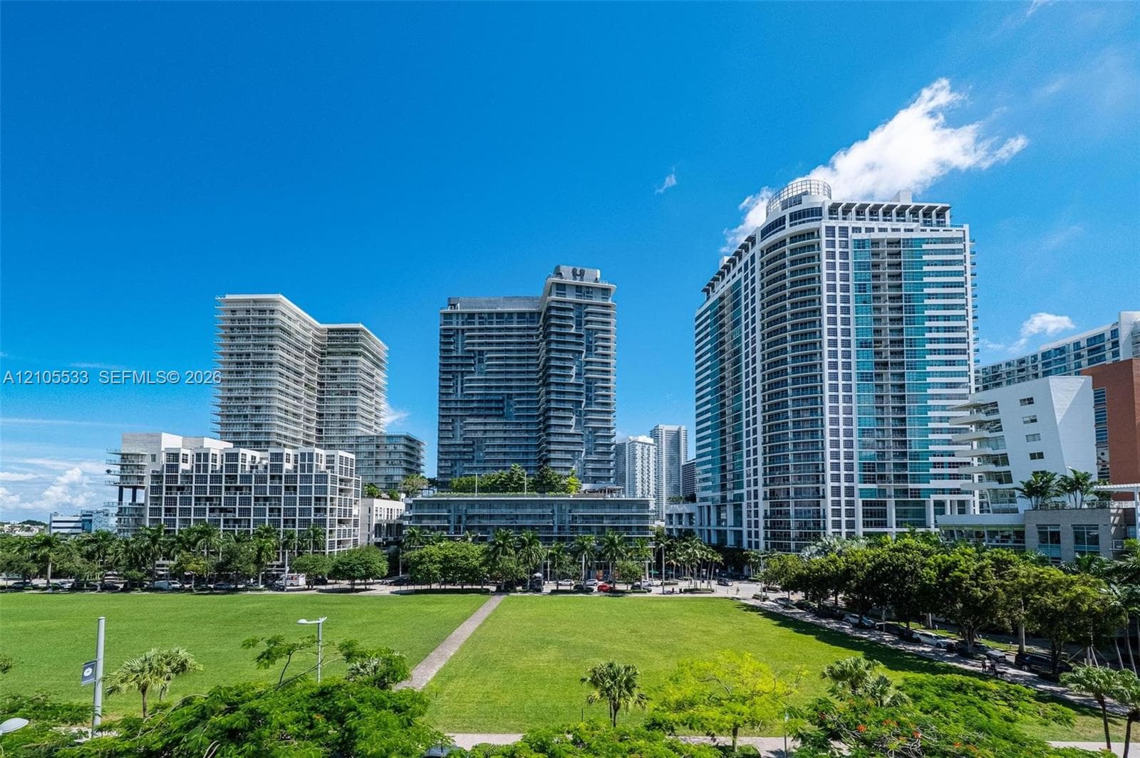 Expansive urban green space bordered by high-rise structures and mature palm trees